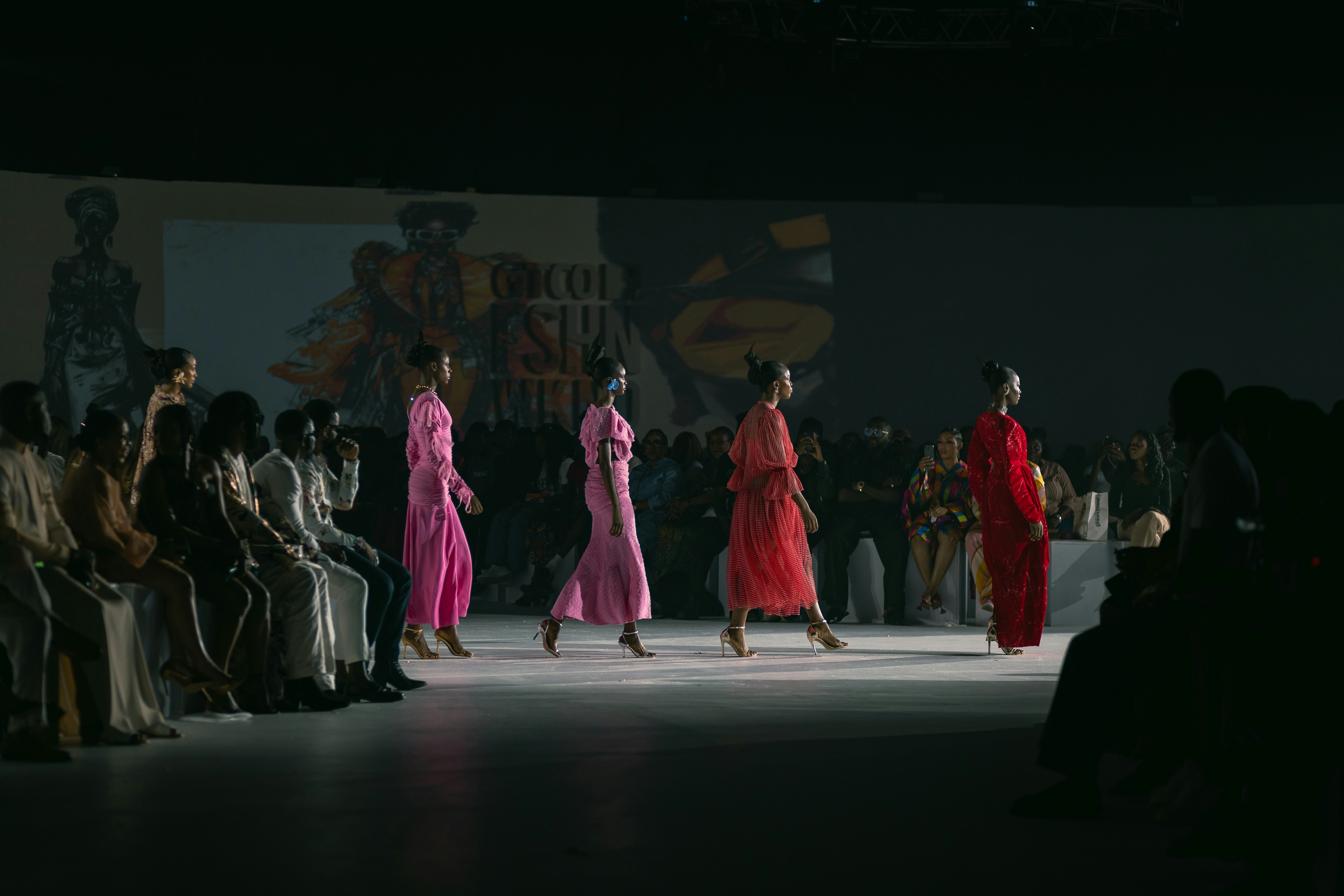 Models in colourful contemporary designs walk a fashion runway before an audience at a creative industry event.